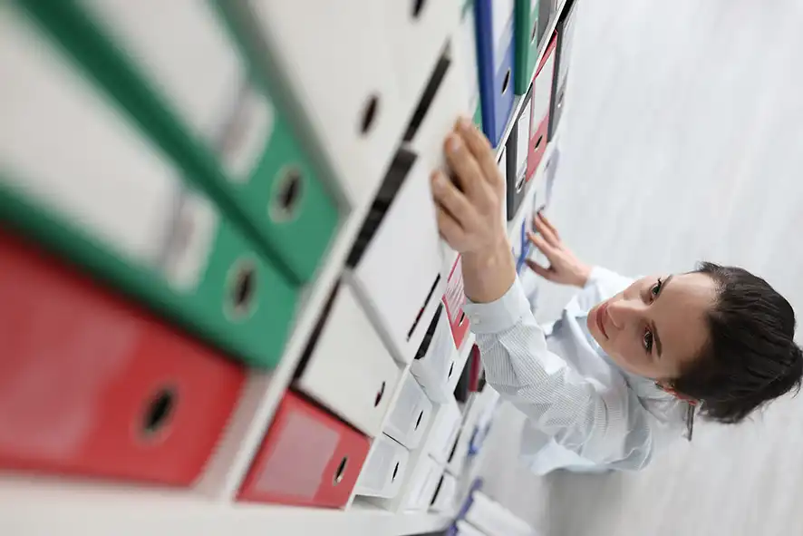 Femme consultant des dossiers administratifs dans une armoire à classeurs – formation autorisations administratives et permis de construire